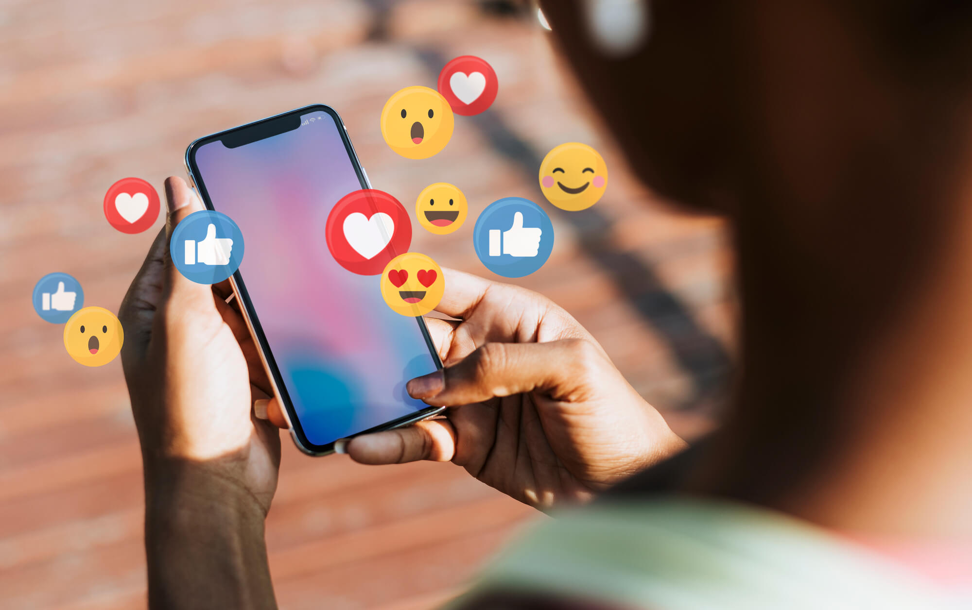 woman holding phone with different facebook reactions coming out