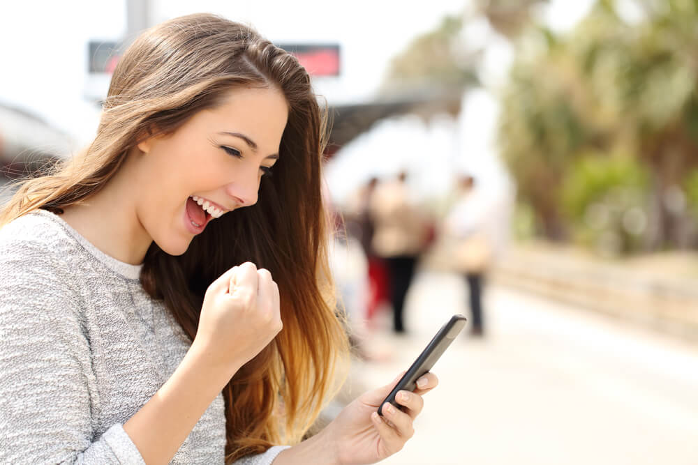 ecstatic woman looking at her phone happy that she won a social media contest held by a Fort Lauderdale SEO Company|