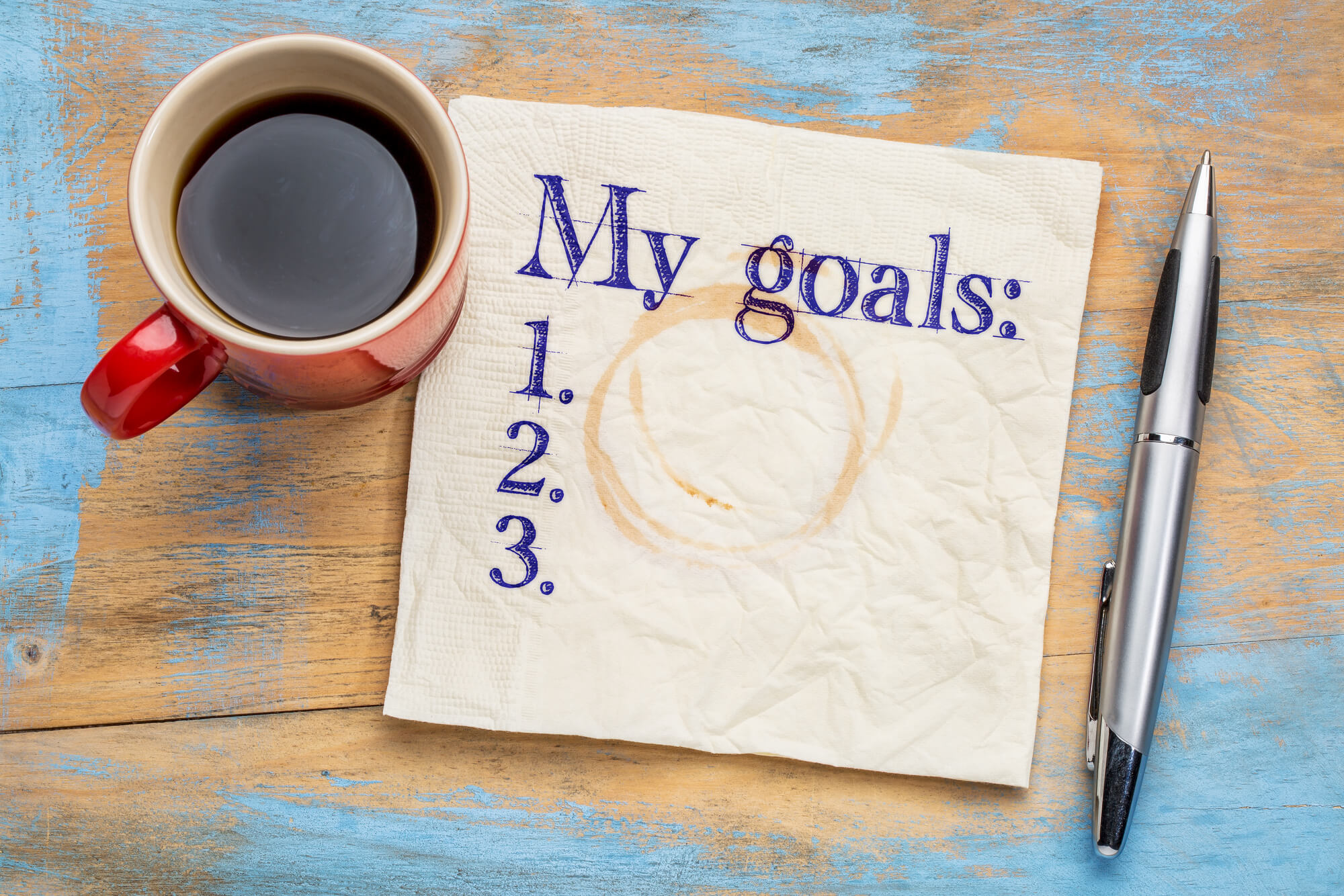 writing goals using a pen and a napkin, with a mug of coffee