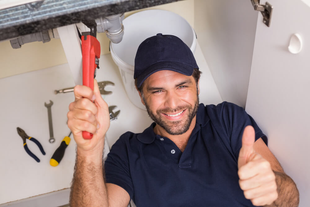 Plumber smiling while fixing client's sink.  