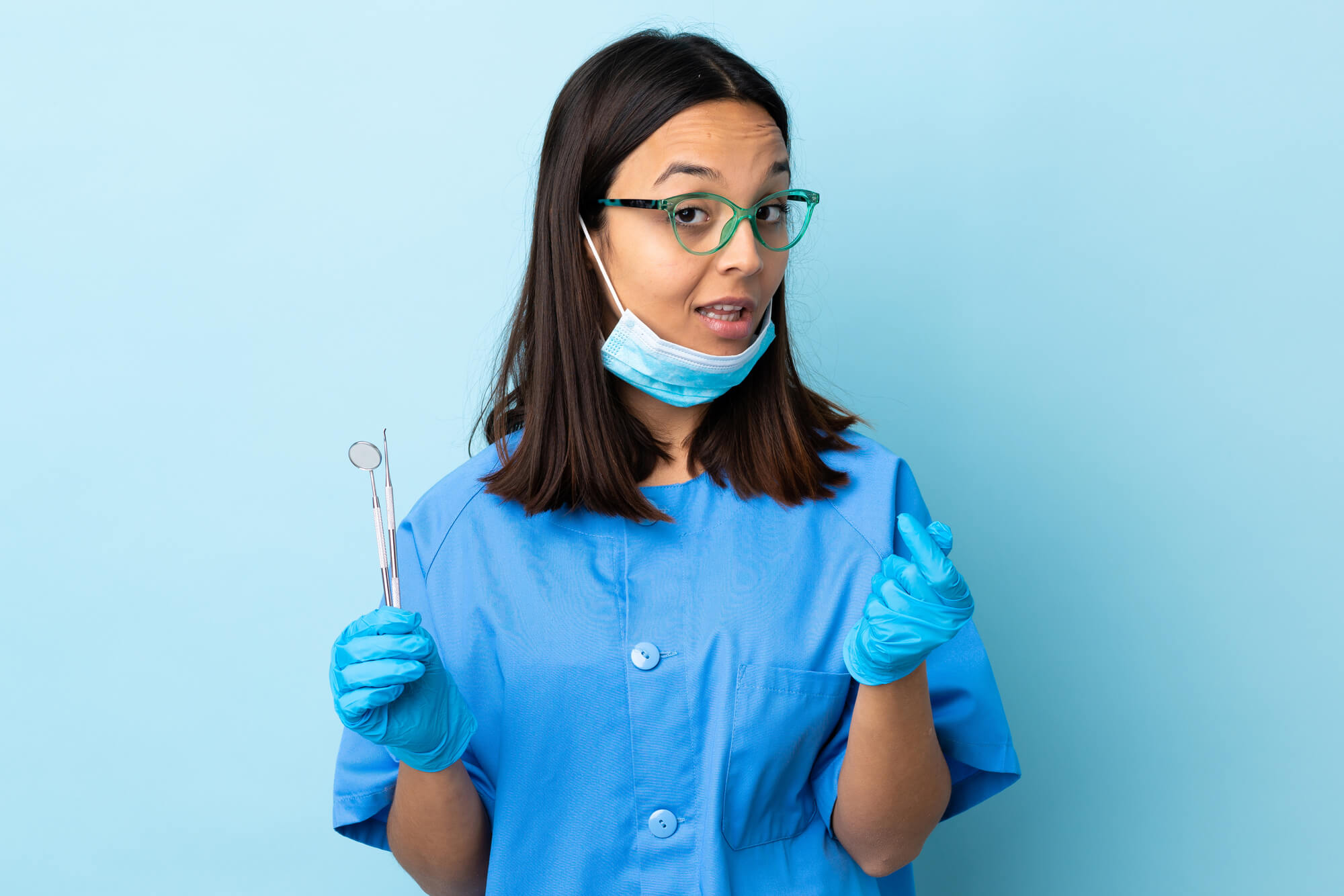 dentist holding dental tools in her right hand and showing a finger heart on the other