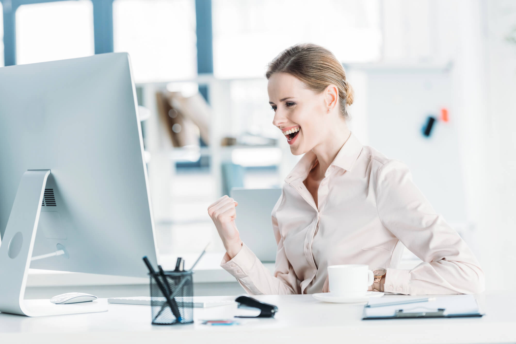 female entrepreneur celebrating while looking at her desktop 