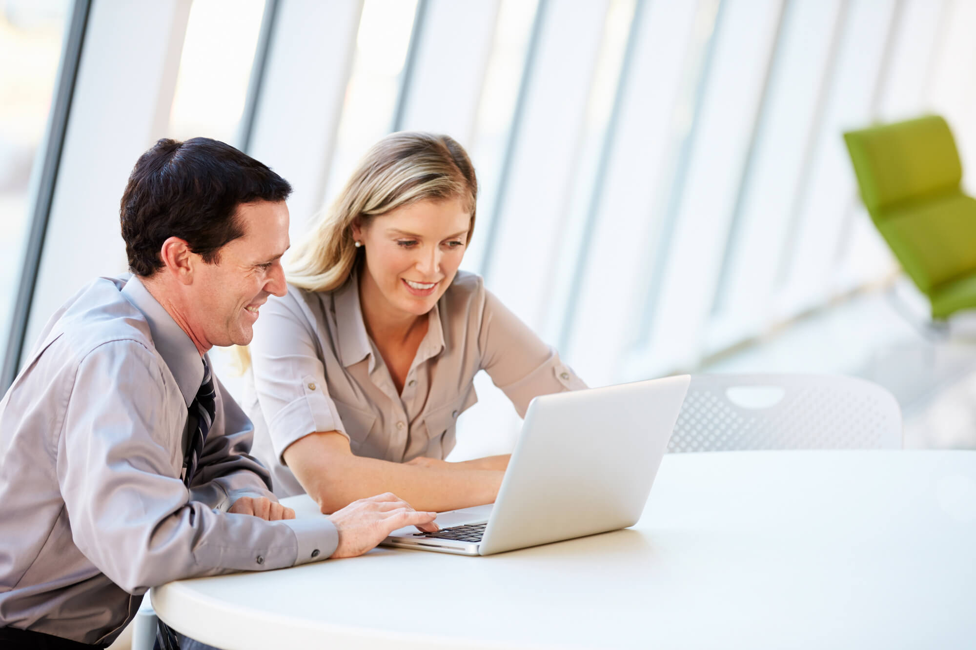 businessman showing female colleague his output on a laptop with both smiling
