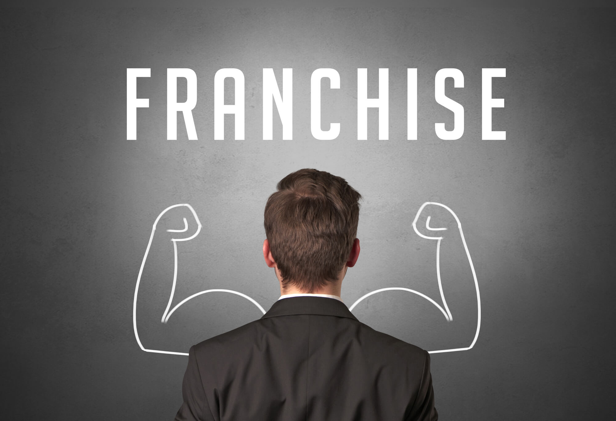 businessman facing a blackboard with the word franchise and a drawing of arms flexing muscles to indicate strength