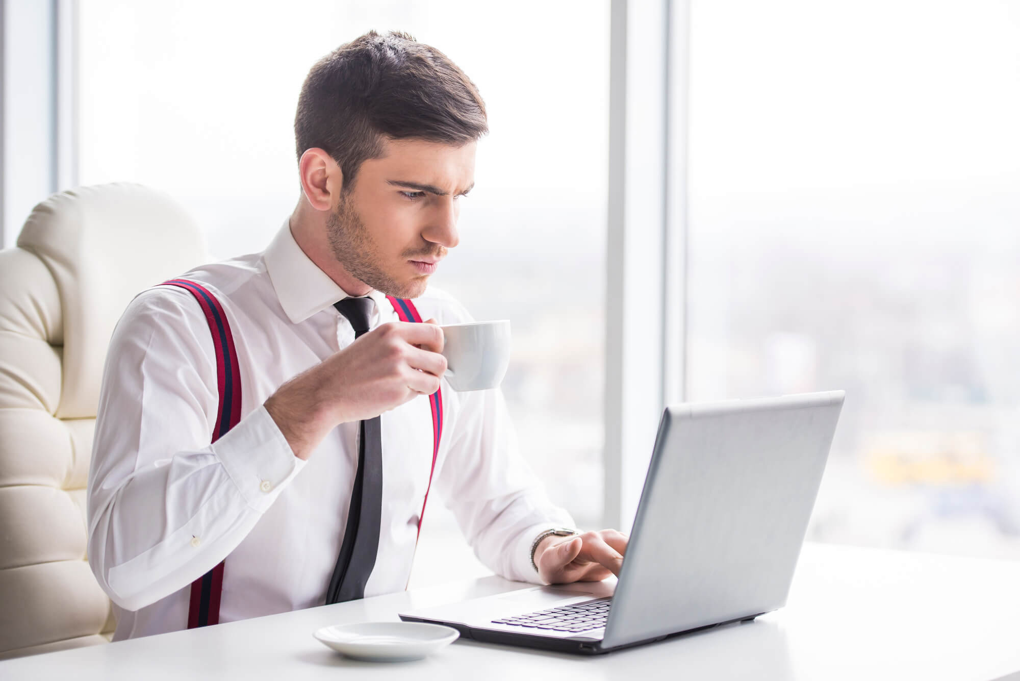 male professional working on laptop while sipping on a cup of coffee