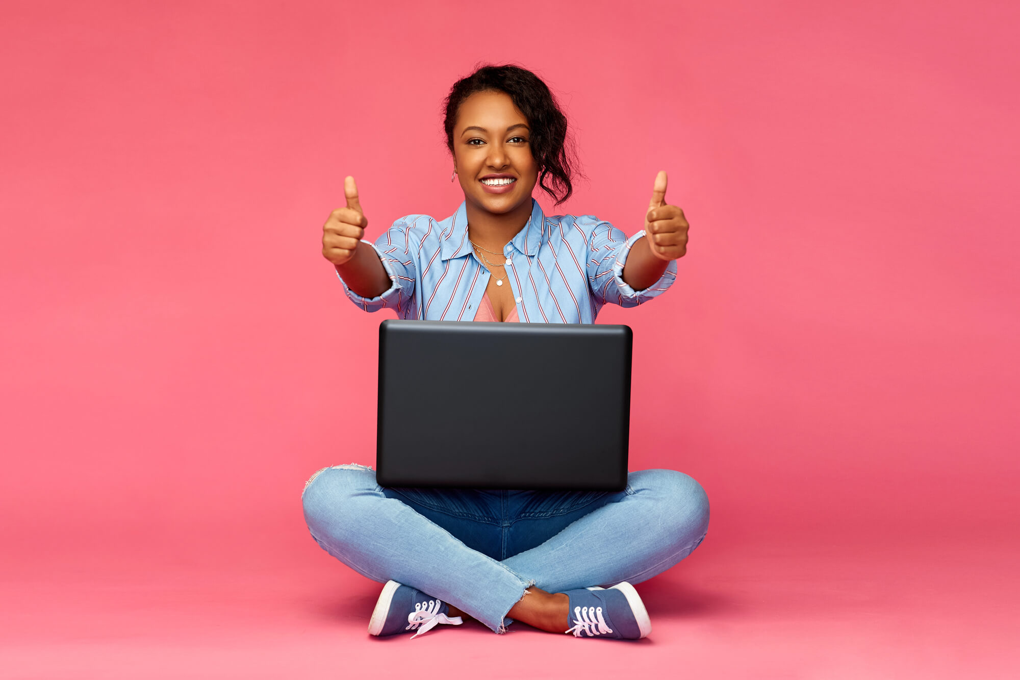 young professional sitting on the floor with laptop on her legs as she gives two thumbs up
