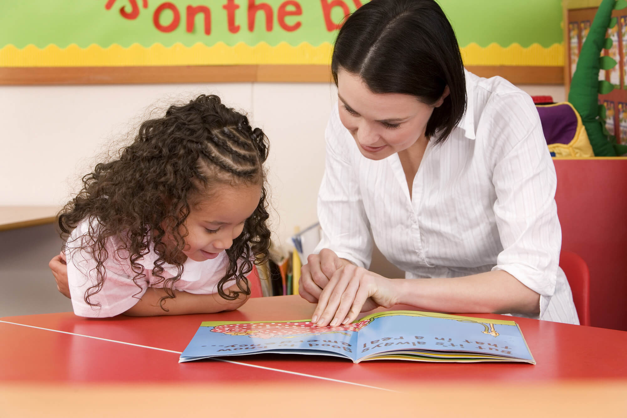 female tutor explaining a book to a little girl