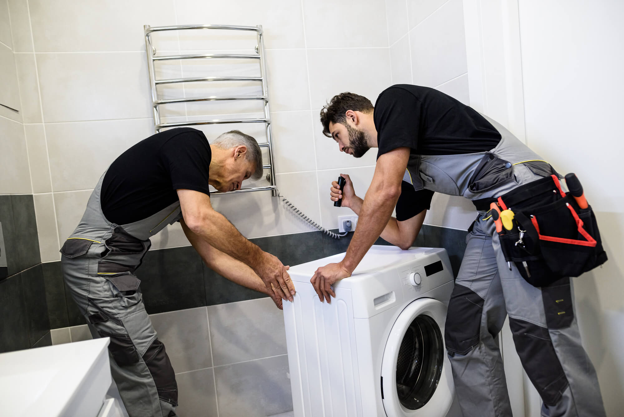 two repairmen in uniform checking a washing machine