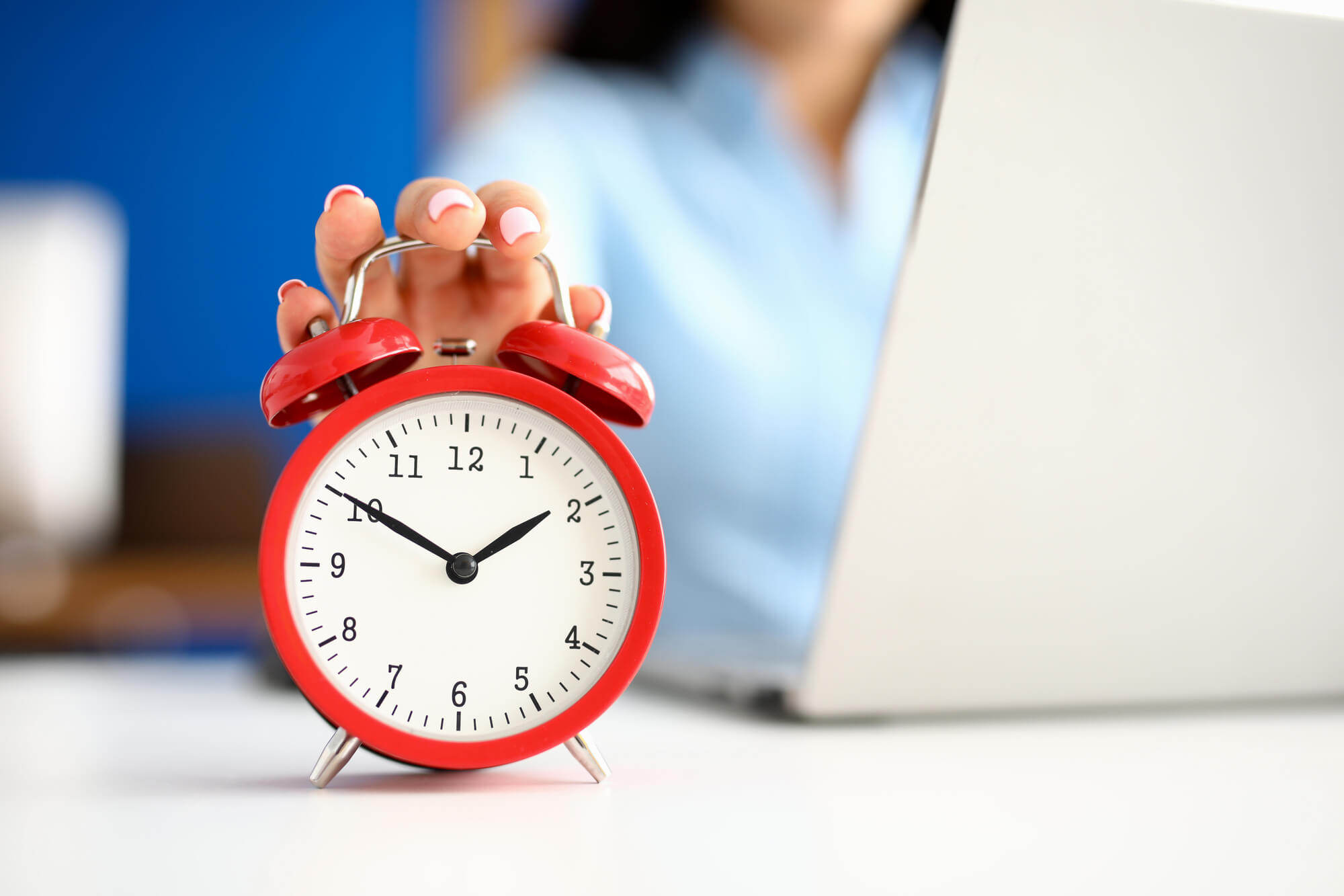 woman touching an alarm clock while working on laptop