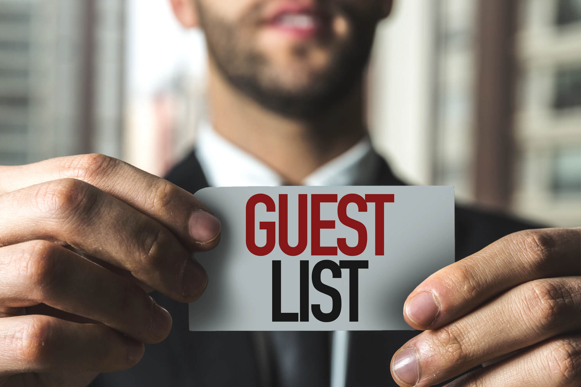 businessman holding card with 'guest list' written on it