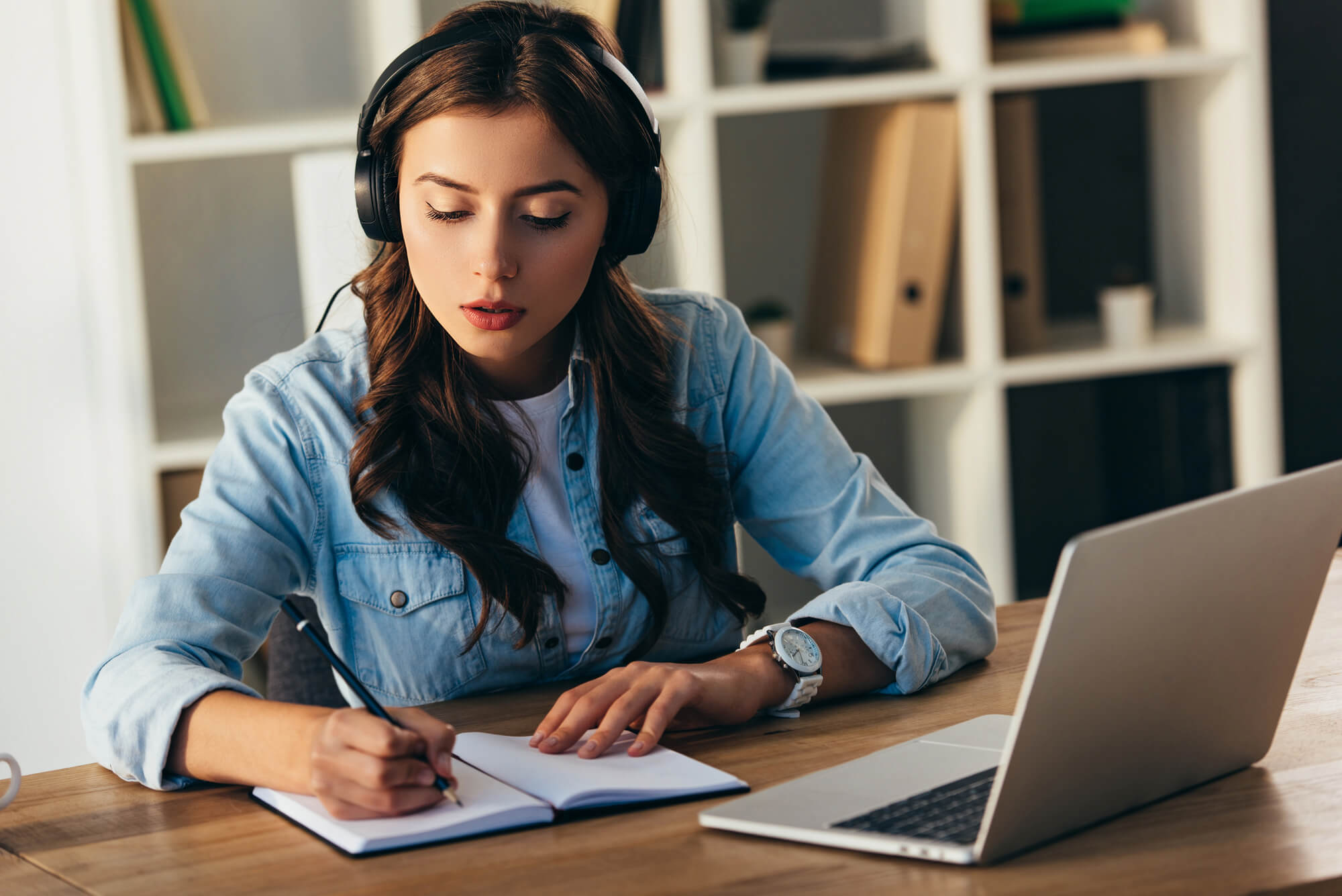 young woman taking notes while watching a webinar on laptop