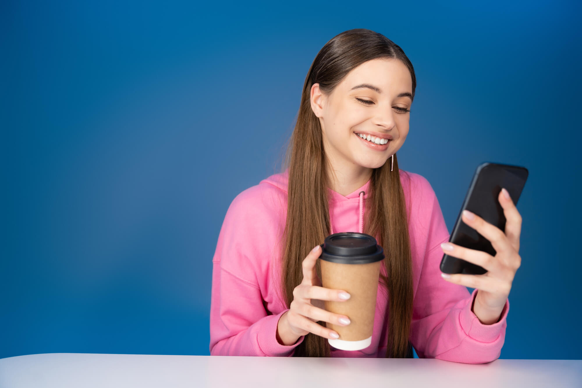 female teen enthusiastically reading on her phone while holding a cup of coffee