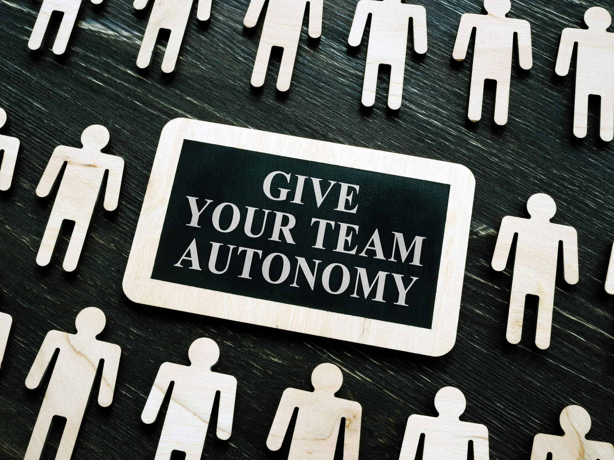 sign saying give your team autonomy surrounded by wooden human figures