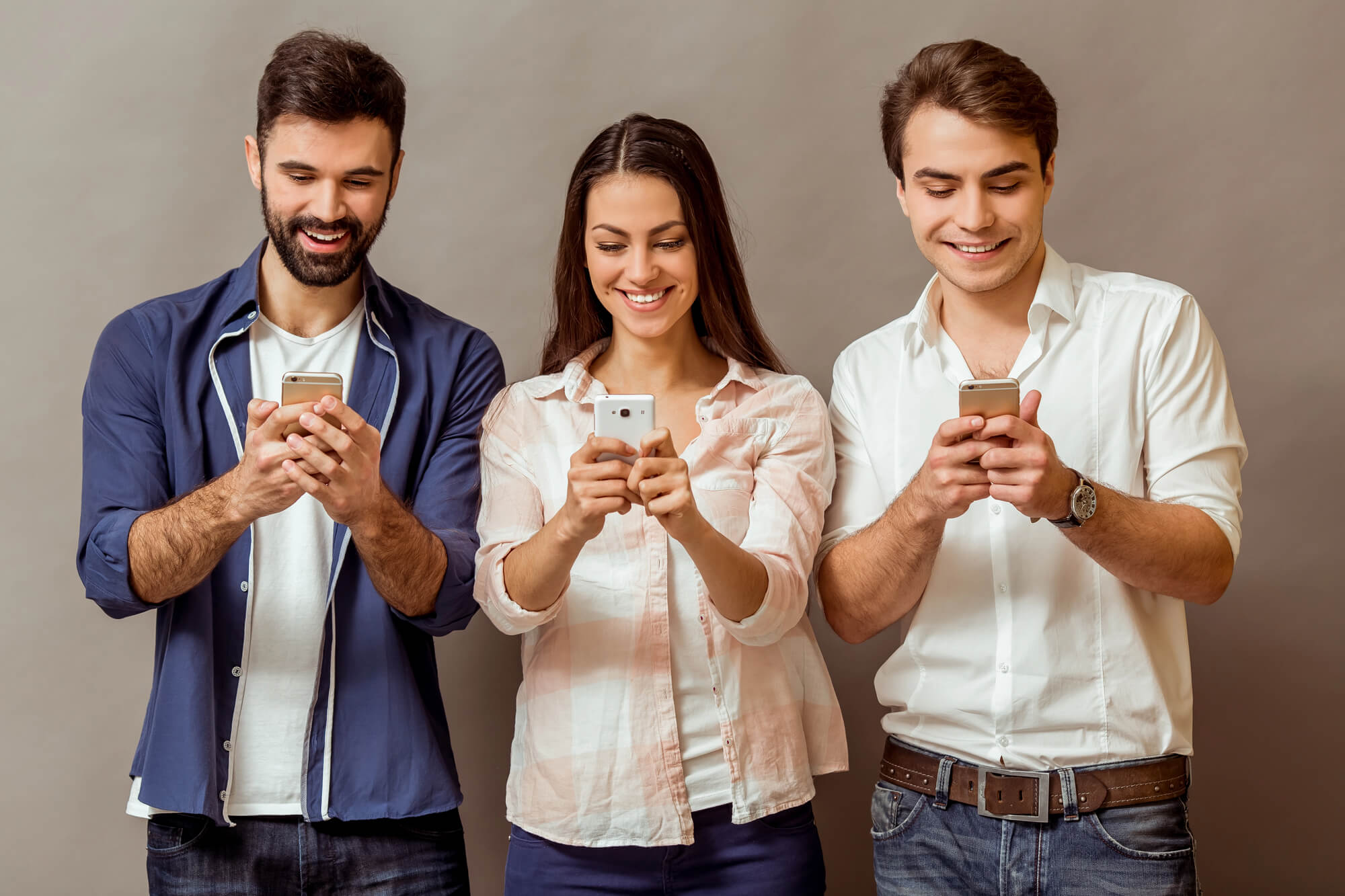 three smiling young adults busy checking their phones 
