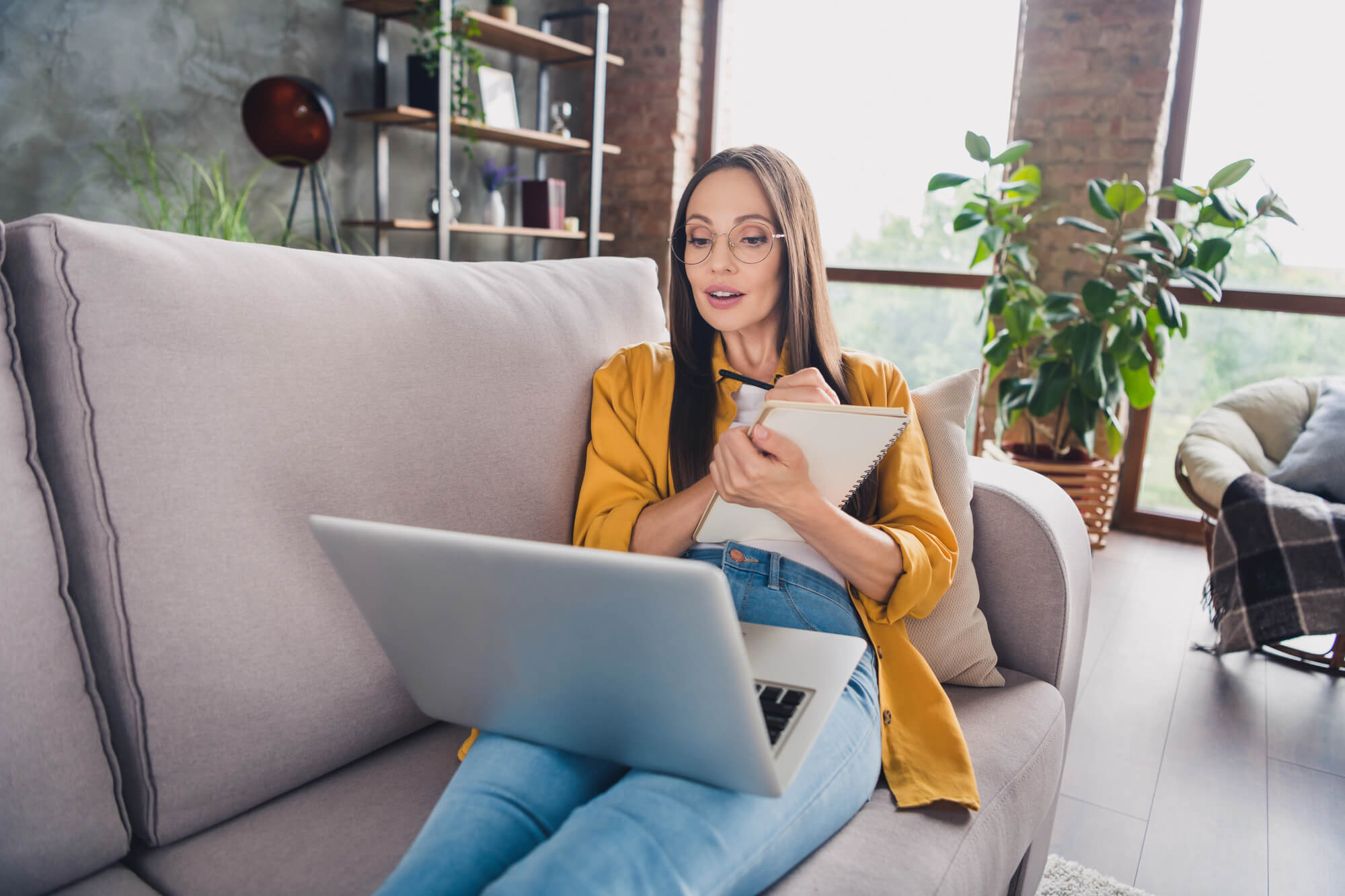woman taking down notes while watching a webinar attentively on laptop