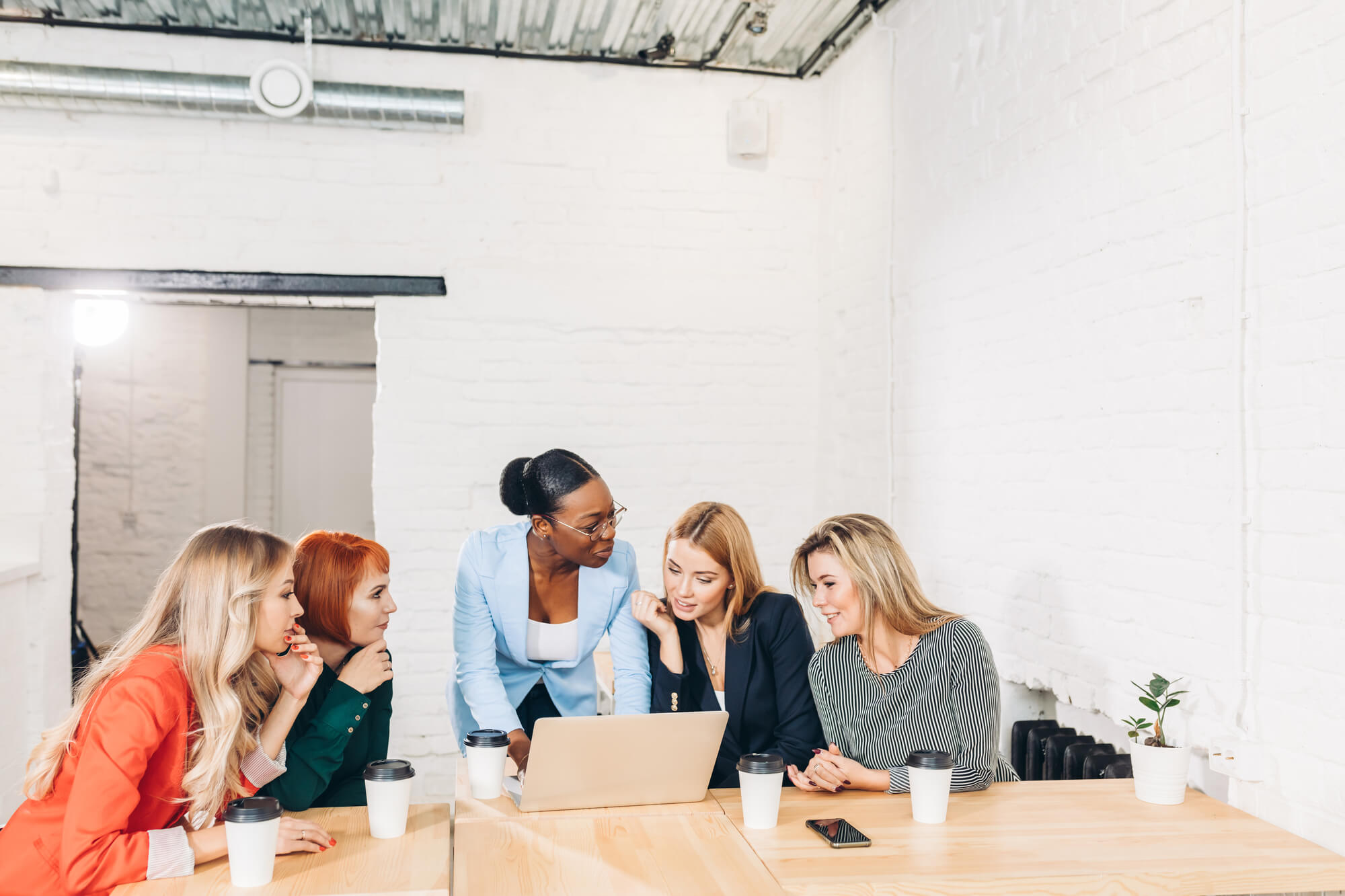 group of women collaborating around a laptop in a bright, modern office space