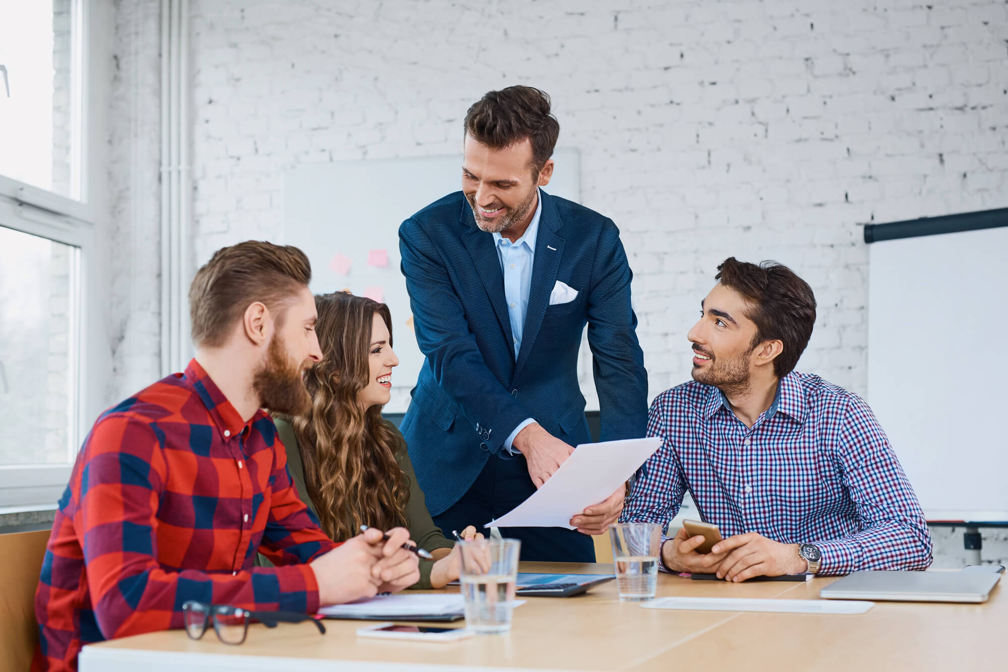 manager discusses a document with three team members seated at a table, all smiling and engaged