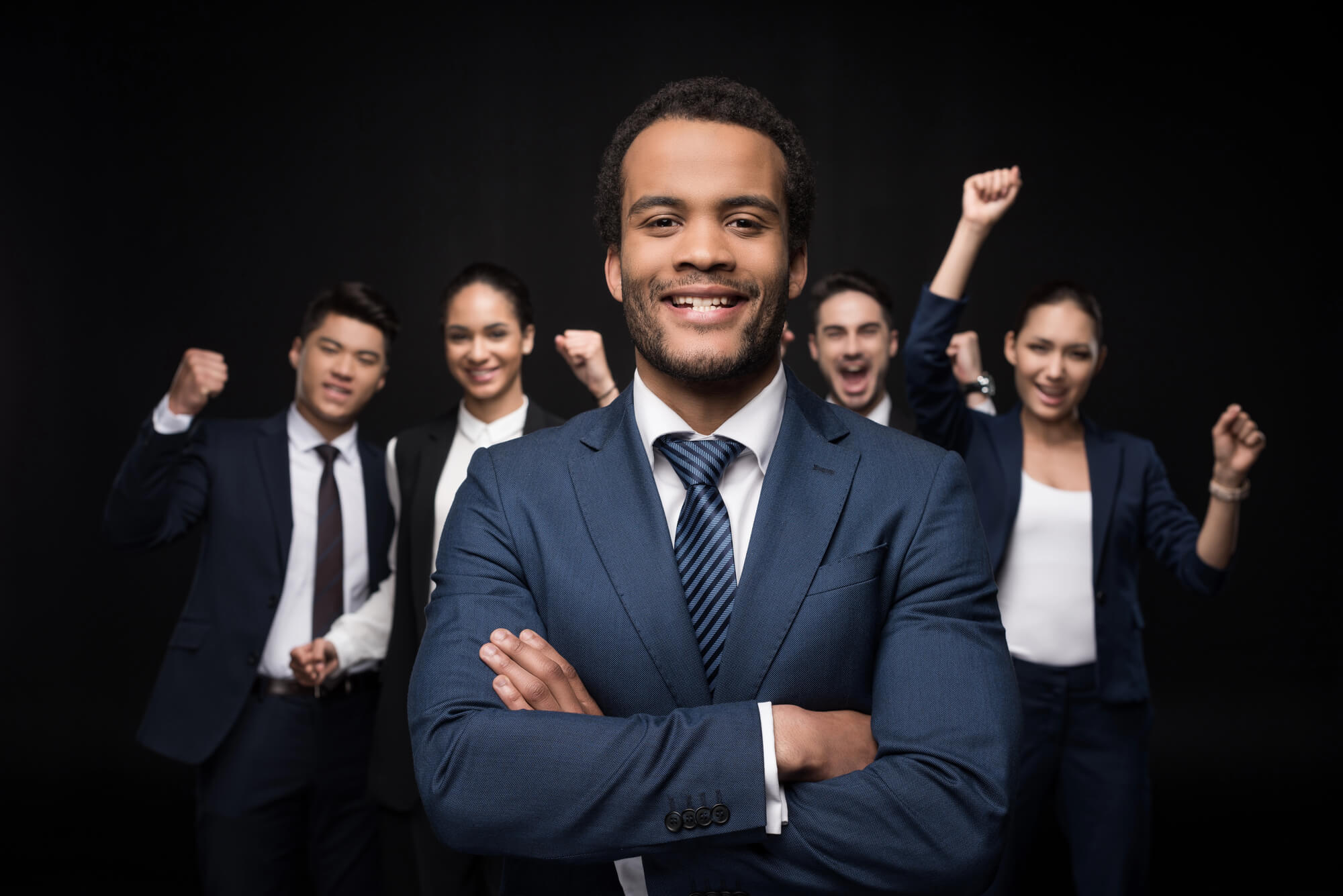 a confident business leader smiles with arms crossed, standing in front of an enthusiastic team celebrating success