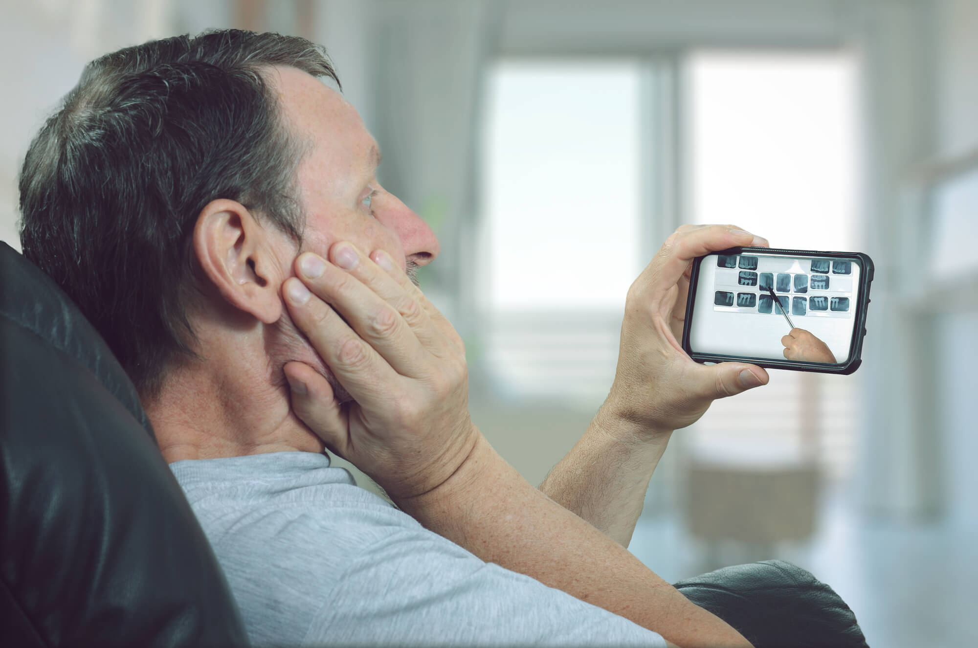 man holding a smartphone during a virtual consultation with a dentist, viewing dental X-rays being analyzed on the screen