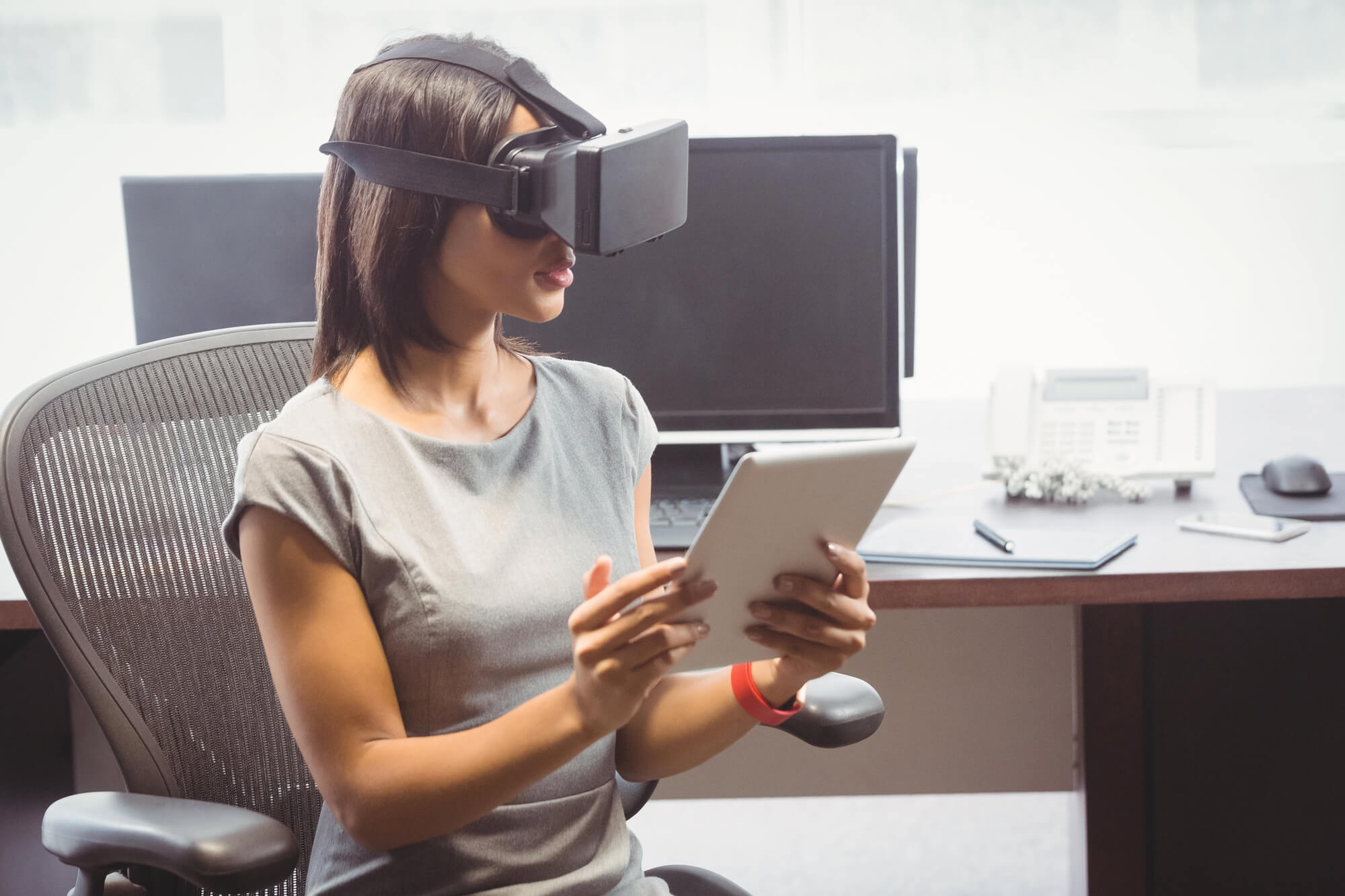 woman in an office wearing a AR headset and holding a tablet