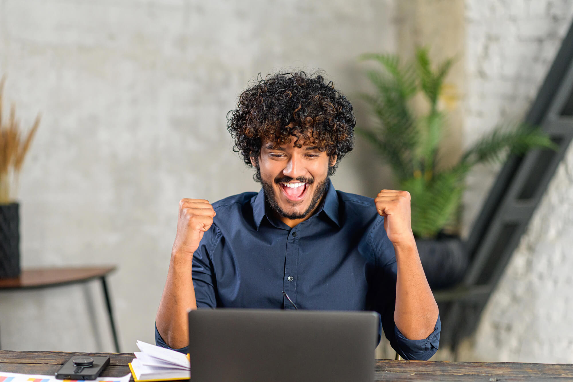 happy male professional celebrating success while looking at his laptop in a modern workspace