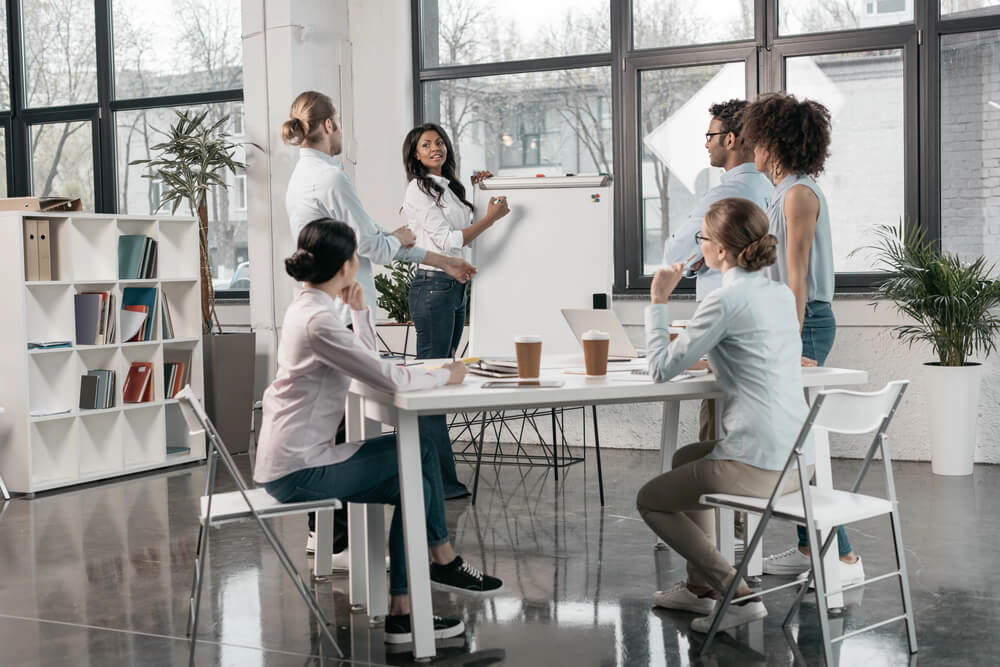 A team meets in a modern office as the leader presents at a whiteboard