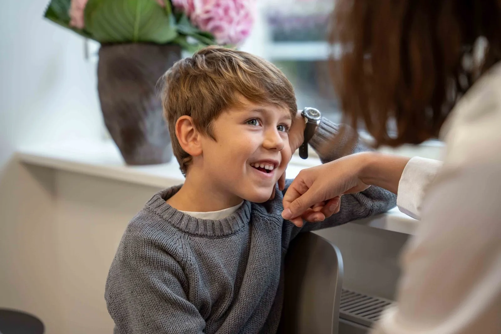 Smilende dreng i grå sweater lytter opmærksomt til en voksen, der taler til ham.