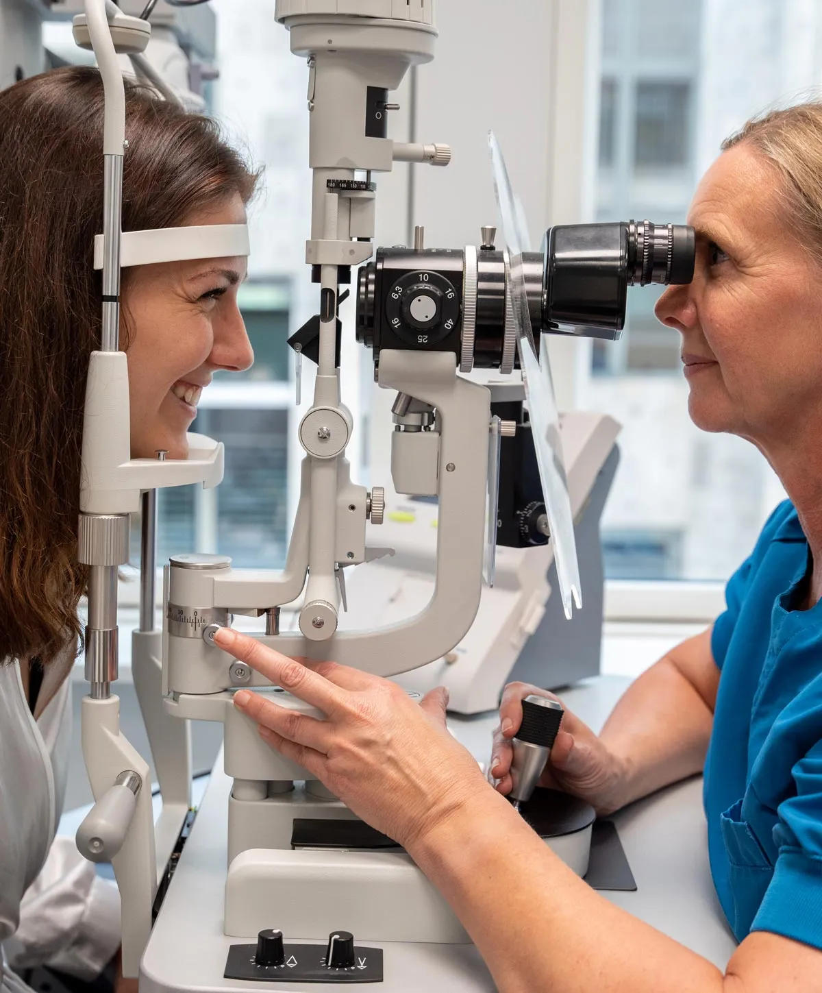 Optiker undersøger kvindes øjne med en spaltelampe i en klinik.