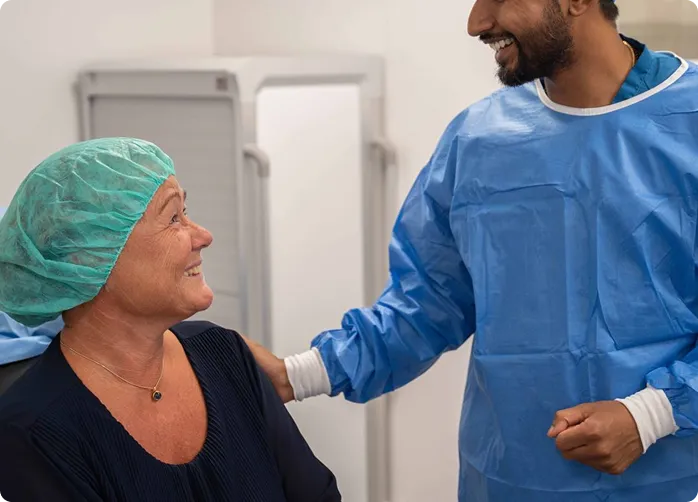 Sundhedspersonale i blå beskyttelsesdragt taler venligt med kvinde iført kirurgisk hætte.