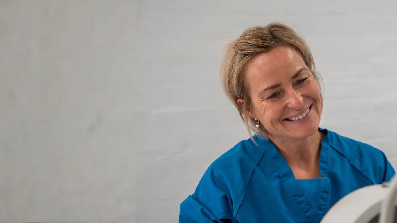 Smilende kvinde i blå medicinsk uniform ser mod et udstyr.