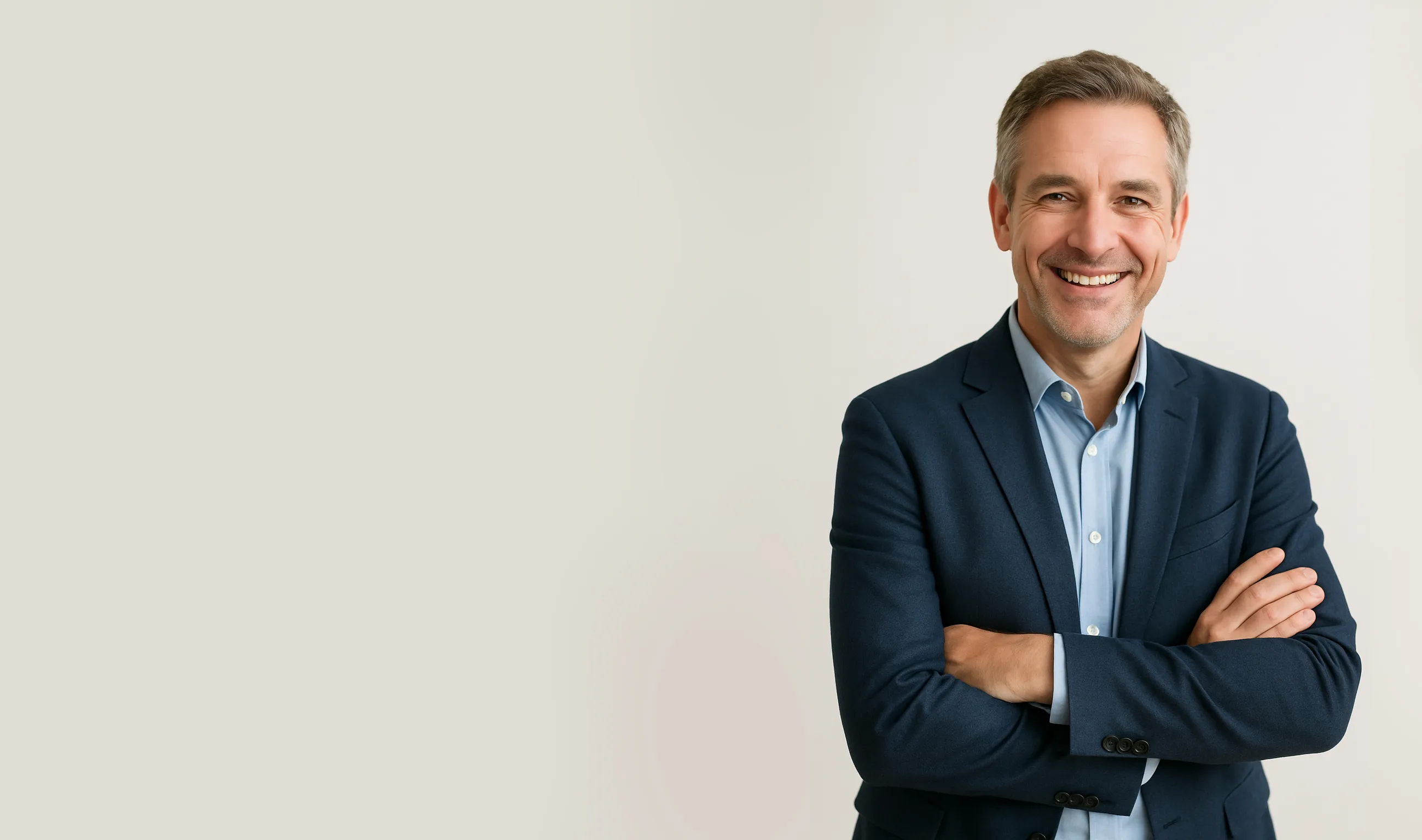 Smilende midaldrende mand med gråt hår iført blå blazer og lyseblå skjorte med armene krydsede.