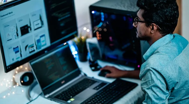 Man working at a desk with two monitors and a laptop.