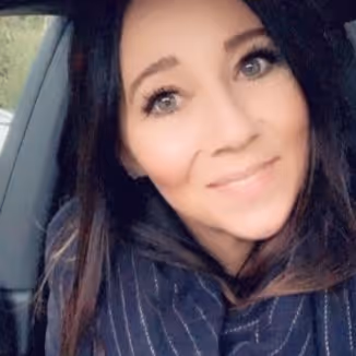 Smiling woman with long dark hair wearing a dark striped scarf inside a car.