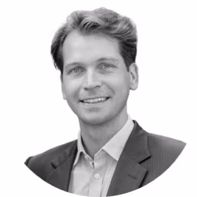 Black and white headshot of a smiling man with light hair wearing a suit jacket and collared shirt.