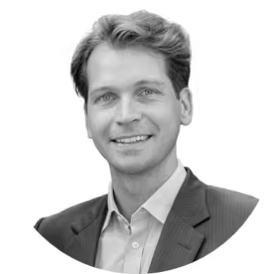 Portrait of a smiling man with light hair wearing a suit jacket and collared shirt against a white background.