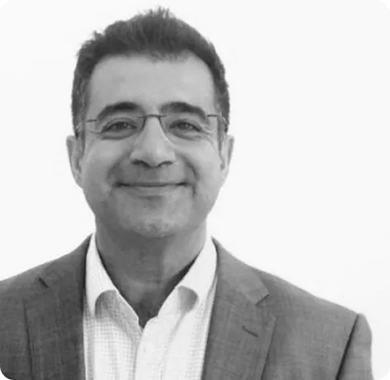 Smiling man with glasses wearing a suit jacket and collared shirt, against a plain white background.