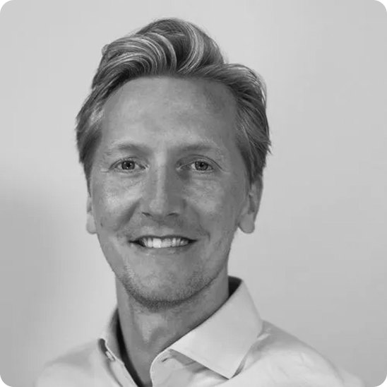 Black and white portrait of a smiling man with light hair wearing a collared shirt against a plain background.