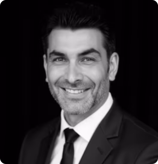 Black and white portrait of a smiling man in a suit and tie with dark hair.