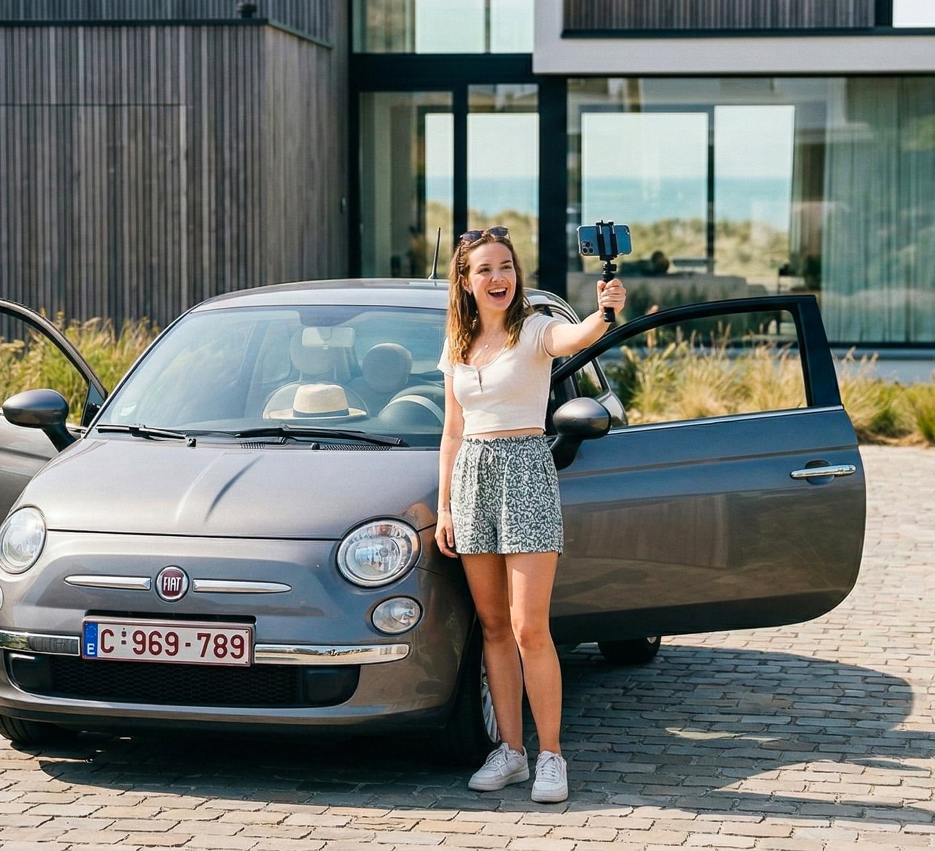 Young couple laughs as man hands car keys to woman next to a red car in a city.