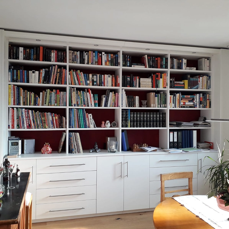 Bücherregal voll mit Büchern, unten mit weißen Schubladen und Türen für geschlossenen Stauraum
