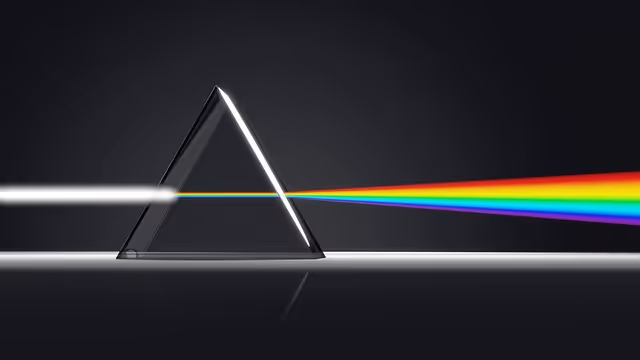Glass triangular prism dispersing white light into a spectrum of rainbow colors on a dark background.