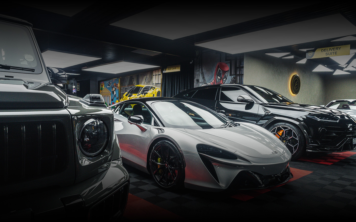 Luxury garage interior featuring a white McLaren sports car, a black Lamborghini SUV, and a gray Mercedes G-Class parked on a checkered floor.
