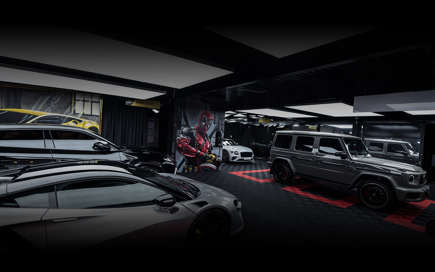 High-end car garage with luxury vehicles including a silver sports car, a black SUV, a white sedan, and a silver SUV under modern lighting and Deadpool wall art.