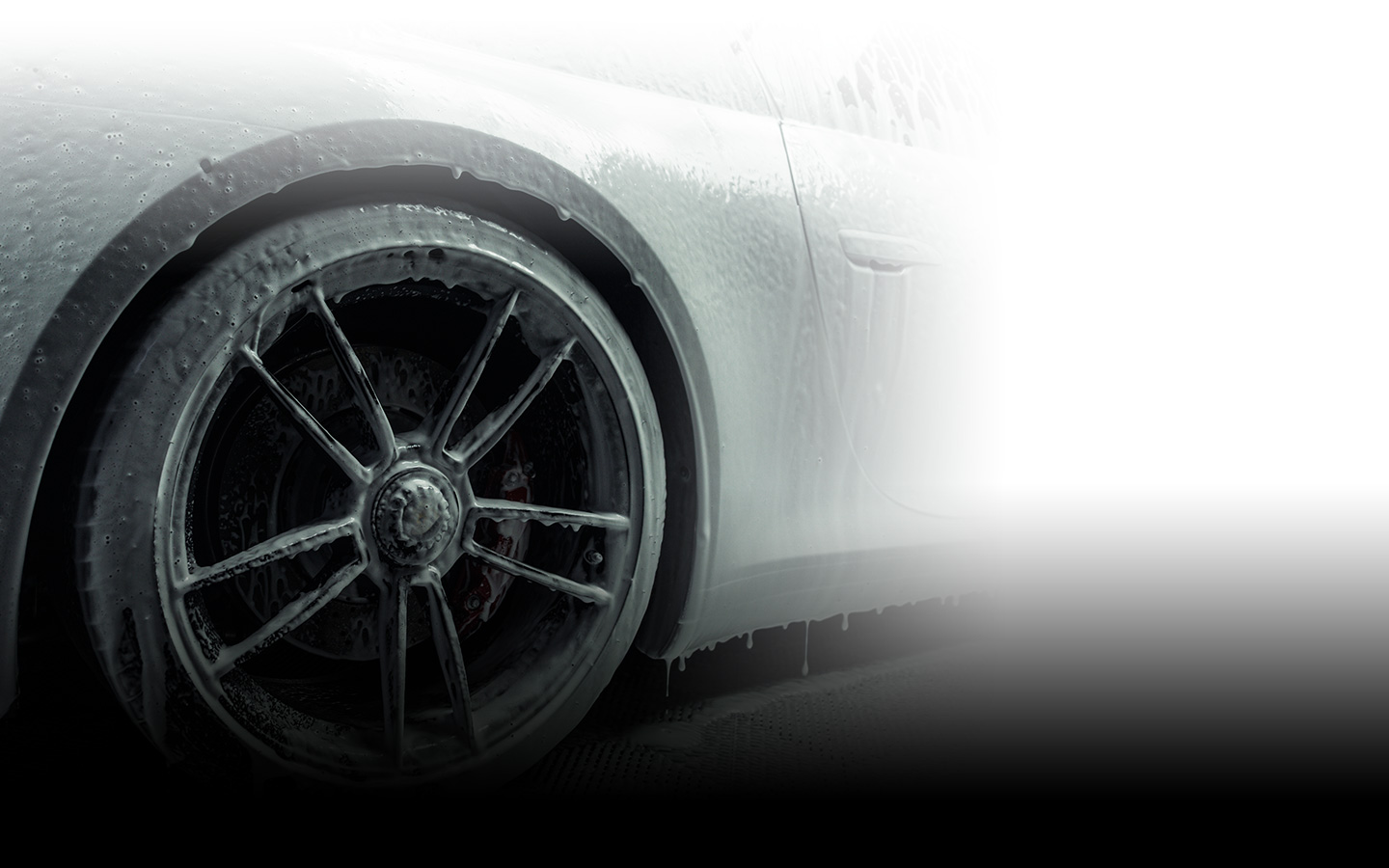 Close-up of a luxury car wheel covered in foam during a wash.