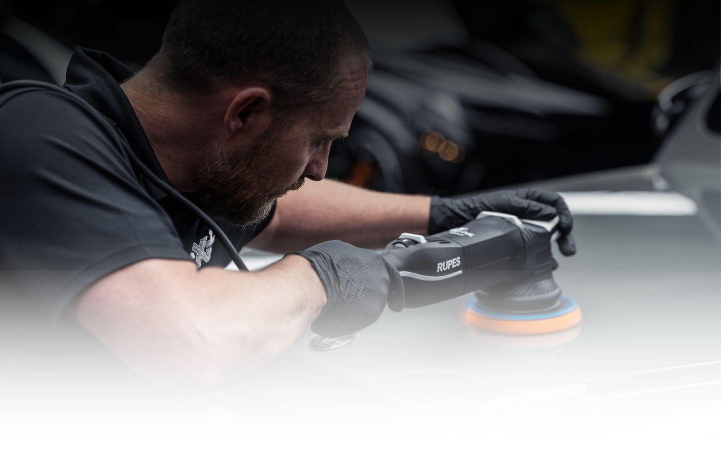 Man using foam cannon to apply thick white foam on a sports car during detailing.