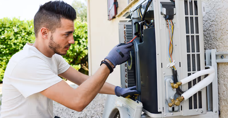 Technician wearing gloves using a screwdriver to repair an outdoor air conditioning unit.