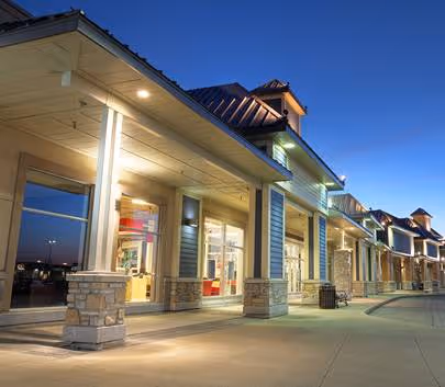 Exterior of a modern retail building with stone pillars and large windows at twilight.