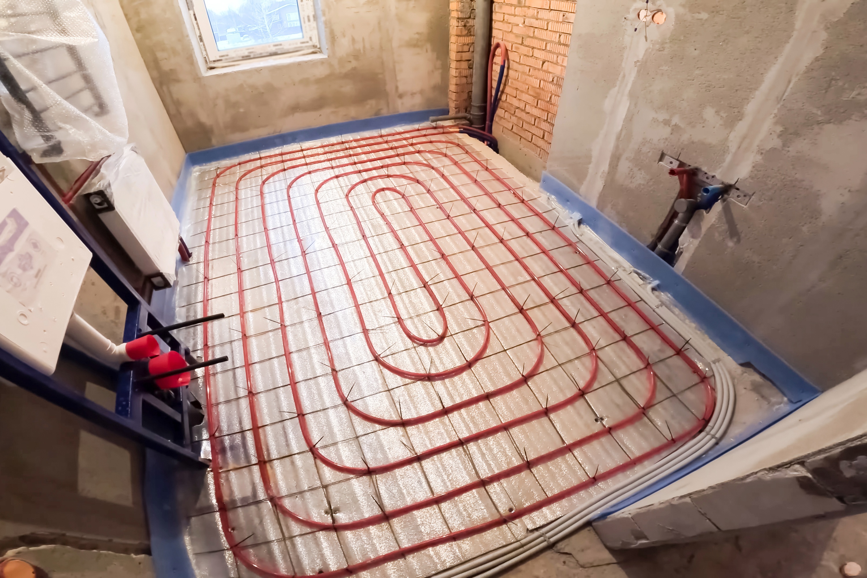 A room under renovation features red underfloor heating pipes neatly arranged on a reflective surface. 