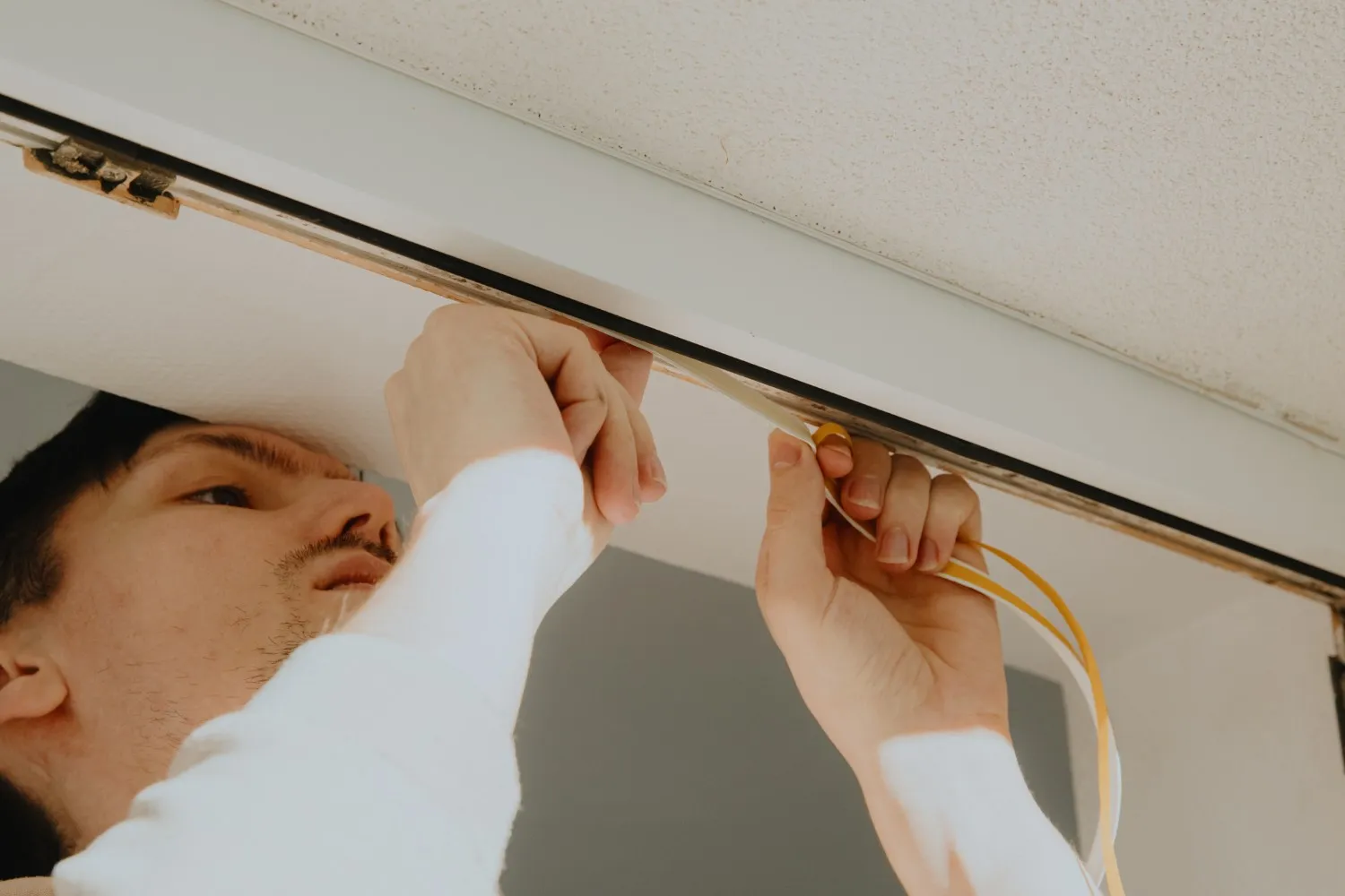 A person installs weather stripping or wiring into a door or window frame during retrofitting.