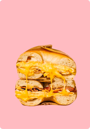 Stacked bagel sandwich halves with melted yellow cheese and bacon on a pink background.